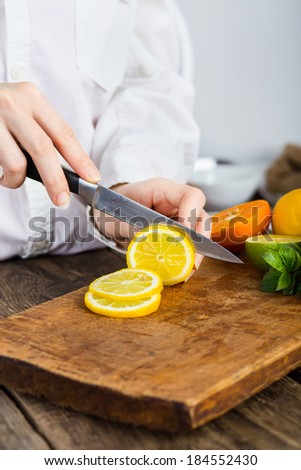 young clean chef hands cutting lemon on old wooden table in kitchen