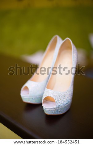 white wedding shoes with a bow and diamonds on a heel on a green, yellow background