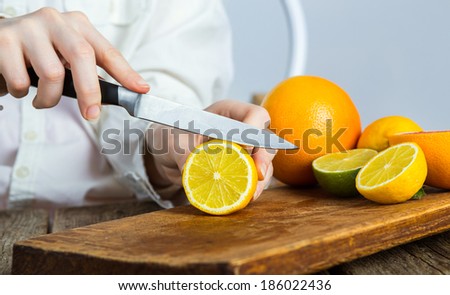 young clean chef hands cutting lemon on old wooden table in kitchen