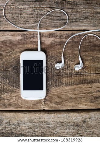 White smart phone with earphones and isolated screen on old wooden desk.