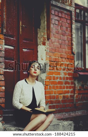 Melancholic woman in classic dress seat near old brick building and read book. Toning photo