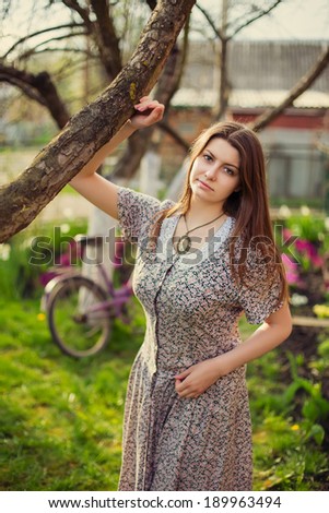Beautiful young woman in dress sitting on grass near old vintage bicycle