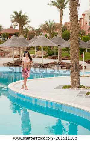 Slender young woman standing hand-to-side near swimming pool
