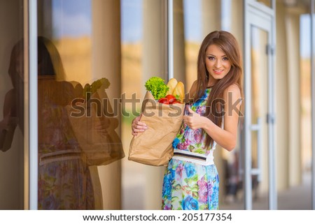 stunning and very beautiful woman in dress with long brown hair holding food in bag near shop