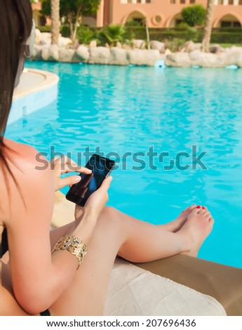 girl in a bathing suit lying on a sun lounger by the pool with a mobile phone with isolated screen