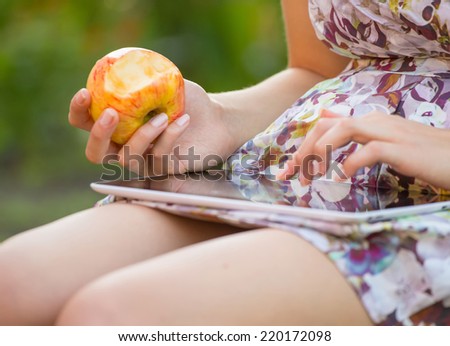 young woman eat apple and play on tablet pc in park