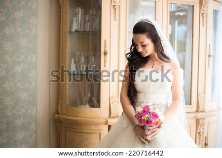 Gorgeous bride in wedding dress in luxury interior with diamond jewelry posing at home and waiting for groom. Romantic rich happy girl in bridal dress