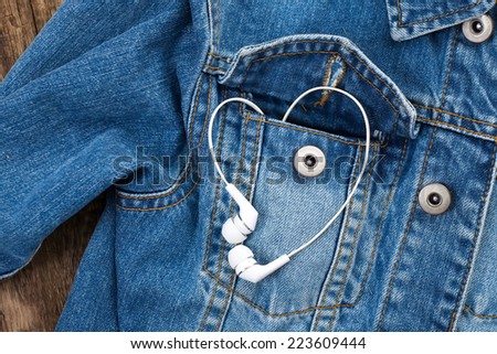 Pair of white ear-in headphones forming a heart shape in a blue pocket denim jacket