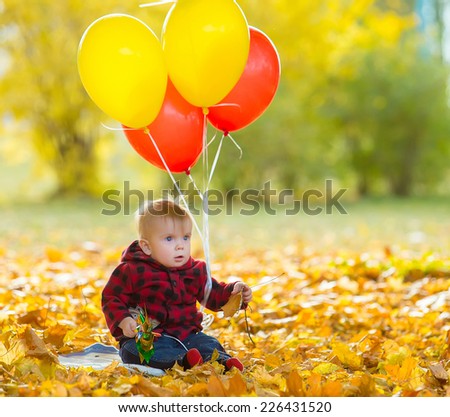 The image of a little child with a bunch of balloons in their hands in yellow autumn park
