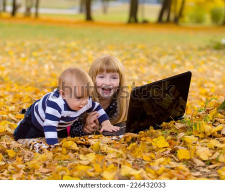 Little smiling girl and brother boy using laptop in a autumn garden