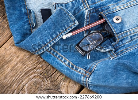 glasses and pencil in pocket of denim jacket on wooden background