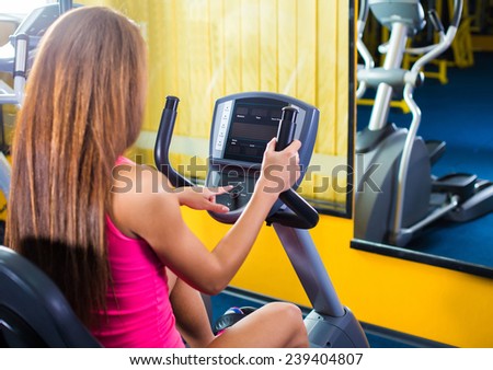 Girl with long hair press start button on bicycle in gym