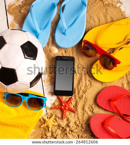 Flip flops, ball, phone, seashell and starfish with tropical flowers on sandy beach