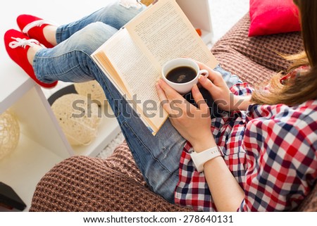 Woman sitting on the sofa reading a book holding her coffee mug in living room at home