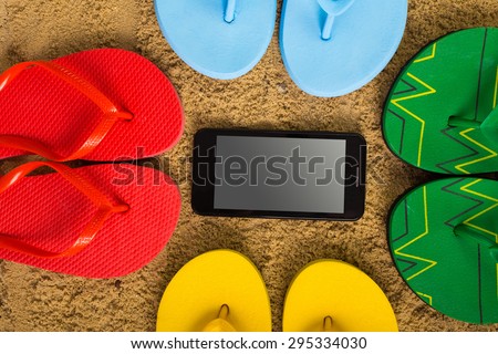Colored Flip flops, phone with earphones on sandy beach