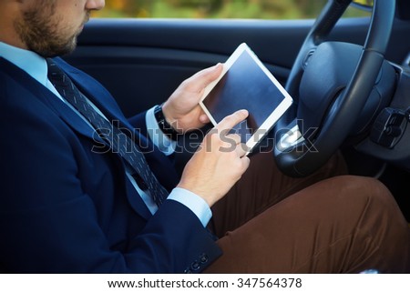 Side view of confident senior man in formalwear sitting in car and hold tablet pc