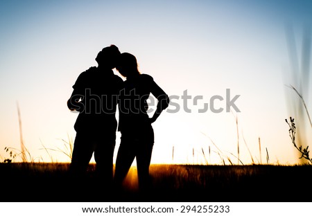 Happy couple silhouette on the meadow during sunset.