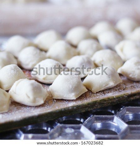 Short-cut siberian pelmeni in the process of cooking, lying in flour on the wooden board near special metallic device