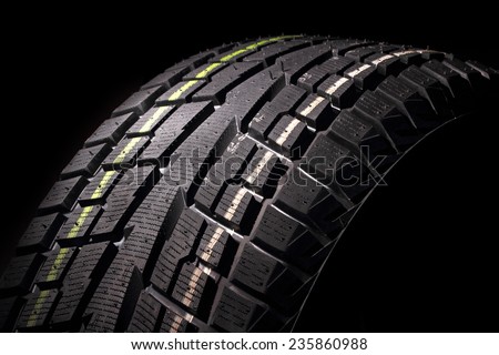 Part of modern non-studded winter tire against black background, studio shot