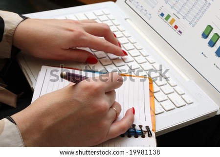 A woman works on a computer and does records in a notebook. Diagram on a screen. Brightly red nails on a hands. Her nails reflected on a screen. 33 years old woman. Selected focus.