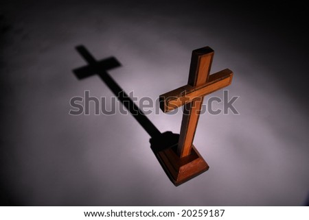 Christian wooden ?ross in light beam. Shadow on background. Religious concept. Black-dark grey background. Little bit blured scene.