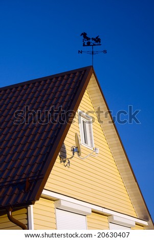 Rural house roof with satellite antenna on a wall and windrose. Clear deep blue sky backdrop. Sunny day.