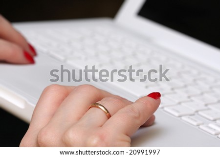 Womanish hands on a white laptop. Brightly red nails. Golden (wedding) ring on a ring-finger. 30 years old woman. Selected focus