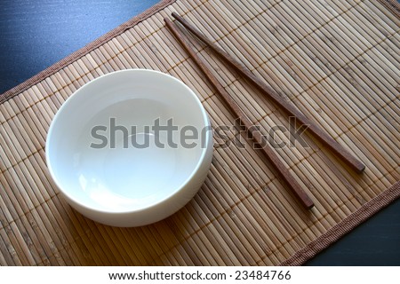Oriental serving. White empty dish and chopsticks on bamboo matt. Above view.