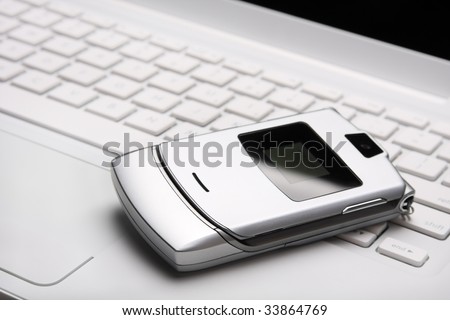 Silver mobile phone on a white laptop. Top view. Selective focus on a phone.