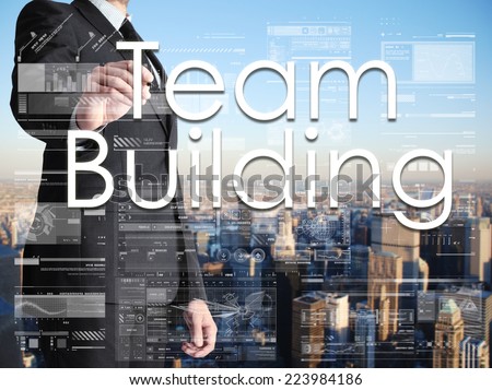 businessman writing Team Building on transparent board with city in background