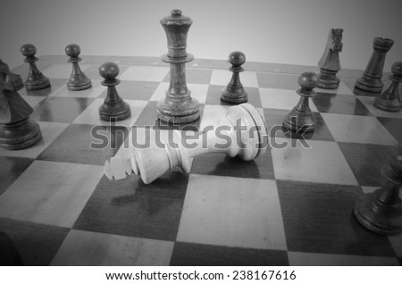 Close-up of a wooden chess table with the black king fallen down, surrounded by white pieces, symbol of lost power or political games