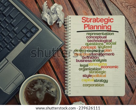 notebook lying on the table with the written words associated with the Strategic Planning , on the table are also laptop and cup of coffee, notes made in the form of the cloud of words
