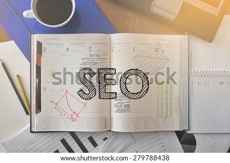 Notebook with text inside SEO on table with coffee, some diagrams on paper and laptop