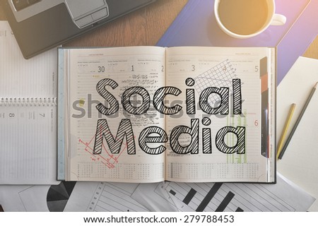 Notebook with text inside Social Media on table with coffee, some diagrams on paper and laptop