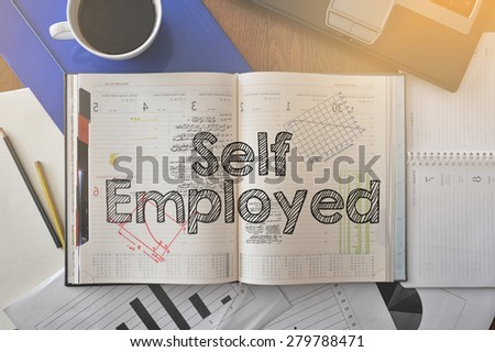 Notebook with text inside Self Employed on table with coffee, some diagrams on paper and laptop