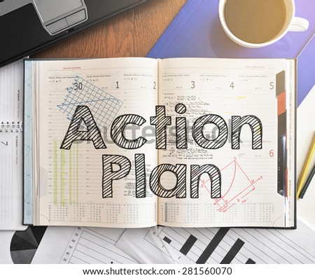 Notebook with text inside Action Plan on table with coffee, laptop and some sheet of papers with charts and diagrams
