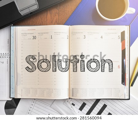 Notebook with text inside Solution on table with coffee, laptop and some sheet of papers with charts and diagrams