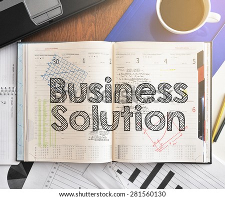 Notebook with text inside Business Solution on table with coffee, laptop and some sheet of papers with charts and diagrams