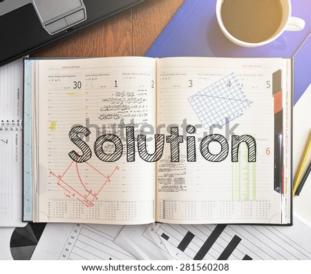 Notebook with text inside Solution on table with coffee, laptop and some sheet of papers with charts and diagrams