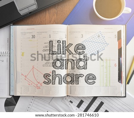 Notebook with text inside Like and Share on table with coffee, some diagrams on paper and laptop