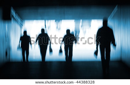 Abstract blur silhouette of people walking out of a dark tunnel into the light. Blue toning.