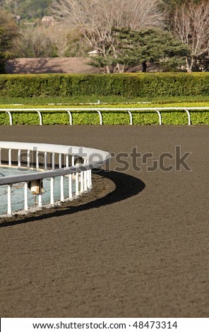Vertical view of horse racing track with white fences and dirt track around the turn.