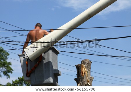 An unidentified man is surrounded by electrical wires as he works high in a basket crane with no safety helmet.