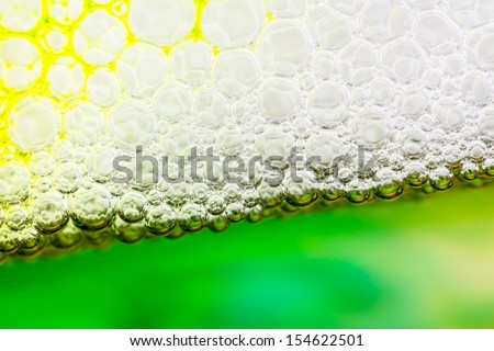 Close up of soap suds floating on water with dye flowing through. Foam against the glass forms geometric pattern.