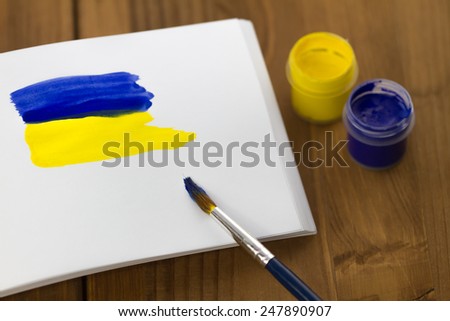 Painted Ukrainian flag on sketchbook with colorful paint tubes and brush on wooden background