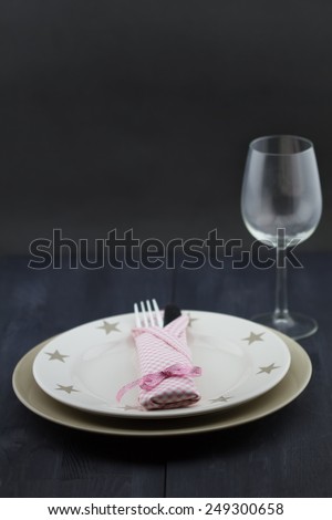 Provence table setting: plate, fork, knife, pink napkin, glass on dark wooden table