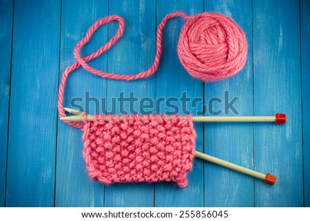 Pink woolen yarn ball and knitting needles on old vintage blue wooden background