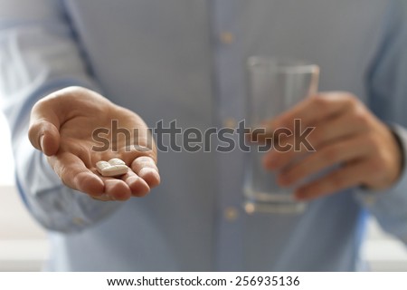 Healthcare and medical concept. Close-up view of man holding pills in one hand and glass of water in the another hand