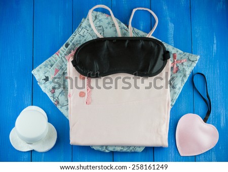 Ready to sleep concept. Top view of female pajamas with blank sleep mask and night cream on blue wooden background
