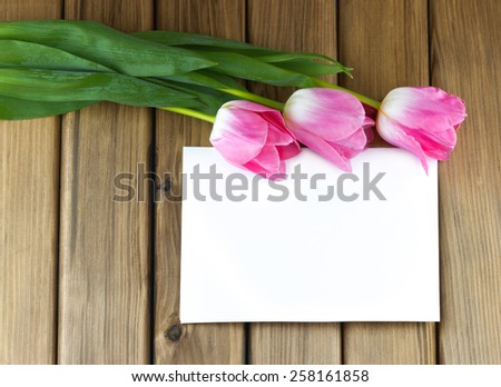 Top view of pink tulips with white sheet of paper on wooden background
